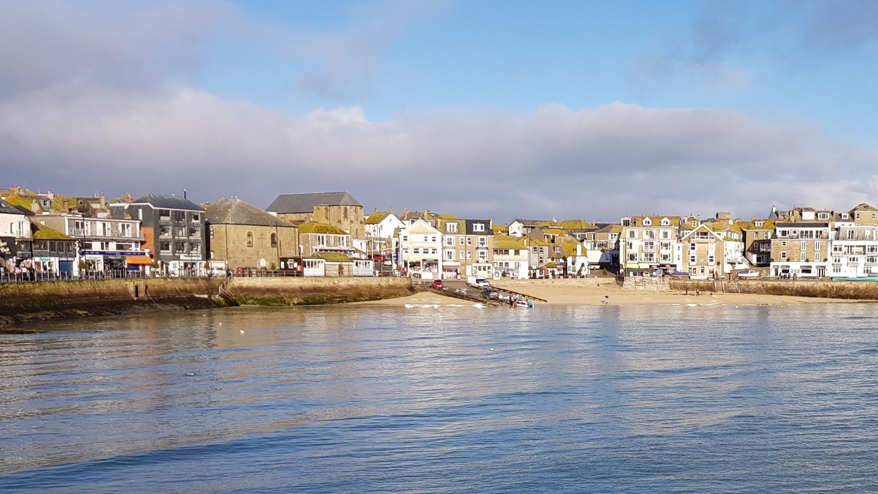 St Ives harbour in Cornwall: waterfront buildings above a sandy beach, with calm water in the foreground