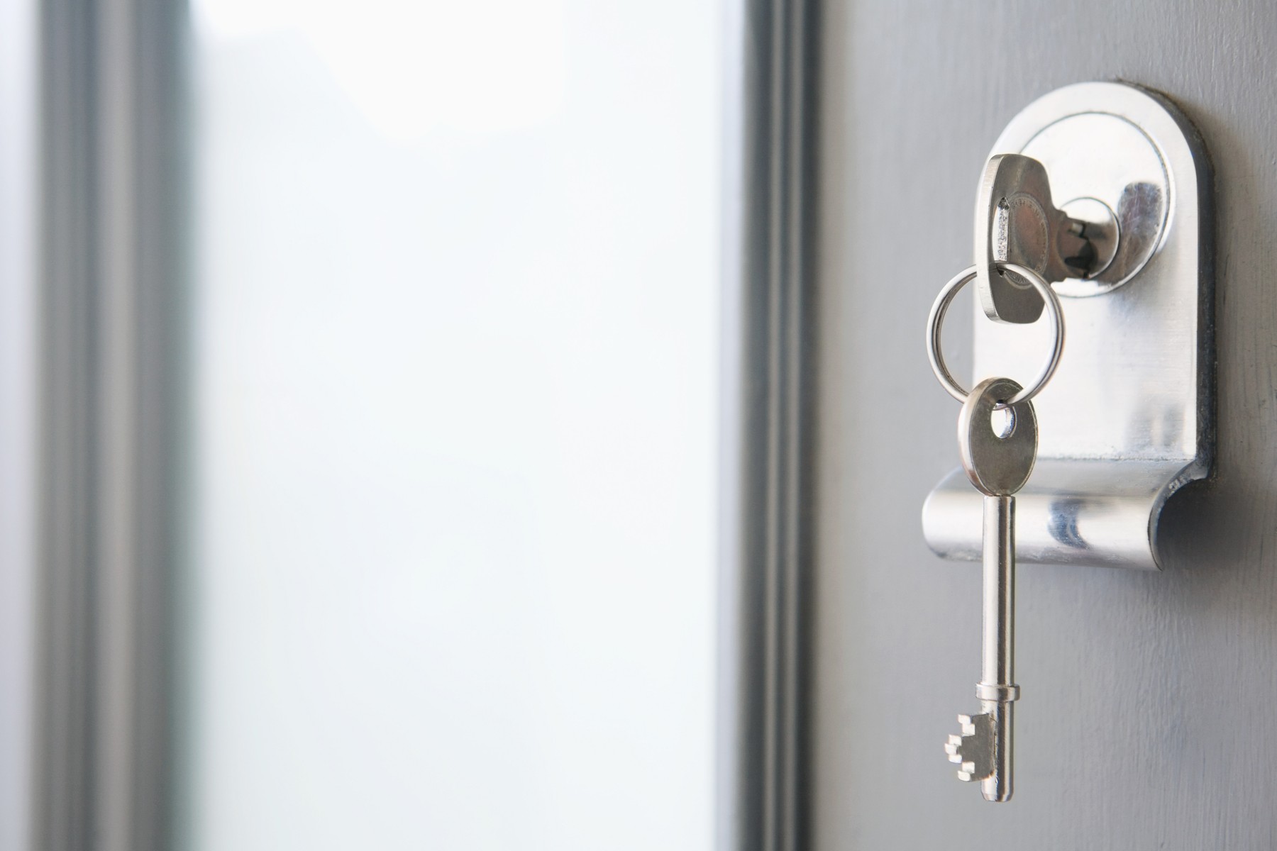 A key on a ring, left in the lock of a grey front door